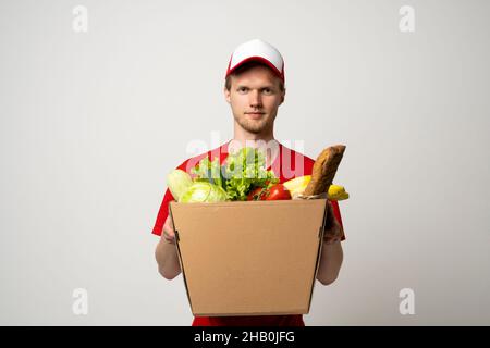 Ein Mann, der ein rotes T-Shirt trägt und einem Kunden zu Hause Lebensmittel liefert. Lieferservice. Stockfoto