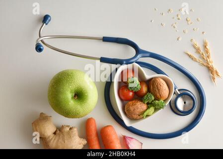 Gesunde Ernährung mit Obst und Gemüse auf weißem Tisch mit herzförmiger Schüssel und Stethoskop. Draufsicht. Horizontale Zusammensetzung. Stockfoto