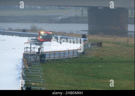 Dresden, Deutschland. 16th Dez 2021. Ein Pistenbully bereitet eine zukünftige Wettkampfstrecke mit Kunstschnee am Ufer der Elbe vor. Am 18. Und 19. Dezember 2021 findet in Dresden der FIS Skilanglauf-Sprint-Weltcup statt. Quelle: Sebastian Kahnert/dpa-Zentralbild/dpa/Alamy Live News Stockfoto