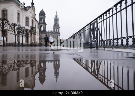 Dresden, Deutschland. 16th Dez 2021. Passanten spiegeln sich in einer Pfütze auf der Brühlschen Terrasse vor der katholischen Hofkirche. Quelle: Sebastian Kahnert/dpa-Zentralbild/dpa/Alamy Live News Stockfoto