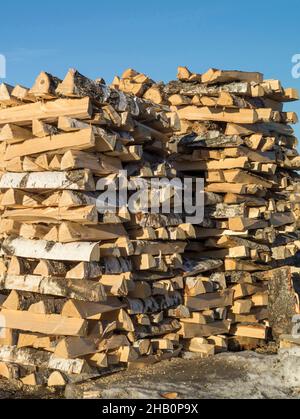 Gespitztes Brennholz, das in einem Stapel von Holzstämmen auf dem Hintergrund des blauen Himmels gebaut wurde. Stapel von Holzkeilen für den Backofen Stockfoto