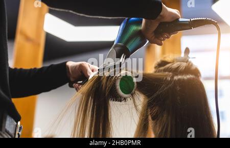 Friseurmeisterin trocknet die Haare des Mädchens mit einem Haartrockner und Kämmen nach dem Waschen im Schönheitssalon. Stockfoto