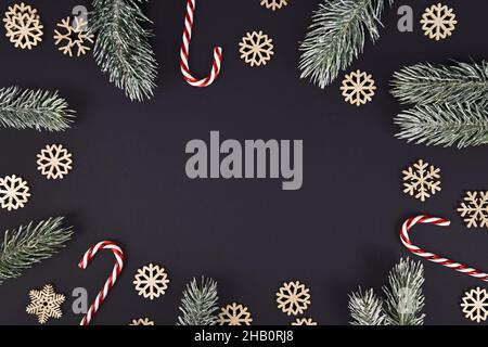 Winter Tannenzweige, Zuckerstöcke und Schneeflocken bilden Grenze um schwarzen Hintergrund mit Kopieplatz Stockfoto
