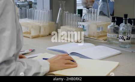 Junger Wissenschaftler Arzt Notizen. Die Wissenschaftlerin notiert sich im Hintergrund die Röhren. Stockfoto