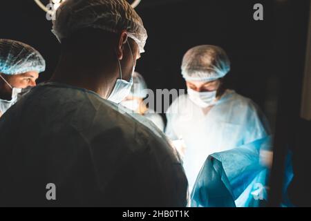 Ein internationales Ärzteteam führt eine komplexe chirurgische Operation an einem unter Anästhesie stehenden Patienten durch. Moderner Operationssaal und erfahrene Chirurgen Stockfoto