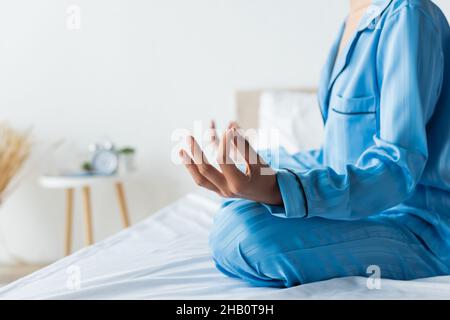 Verkürzte Ansicht einer afroamerikanischen Frau im Schlafanzug, die auf dem Bett meditiert Stockfoto