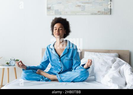 Erfreut afroamerikanische Frau im Schlafanzug meditierend auf Bett Stockfoto