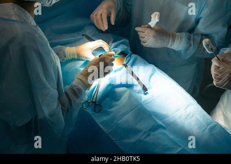 Ein internationales Ärzteteam führt eine komplexe chirurgische Operation an einem unter Anästhesie stehenden Patienten durch. Moderner Operationssaal und erfahrene Chirurgen Stockfoto