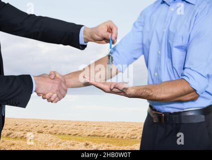 Mittelteil des Immobilienmaklers, der einem Mann Schlüssel gegen Grasfeld und blauen Himmel gibt Stockfoto