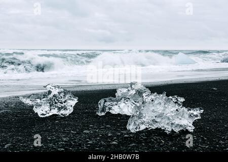 Eisbergstücke am Black Diamond Strand in der Nähe der Jokulsarlon Lagune, Island. Wellen des Atlantiks und wolkige Himmel auf dem Hintergrund. Landschaftsfotografie Stockfoto