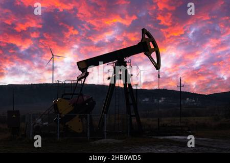 Ölpumpe und Windturbinen gegen den unglaublich violetten Sonnenuntergang. Industriekonzept Stockfoto