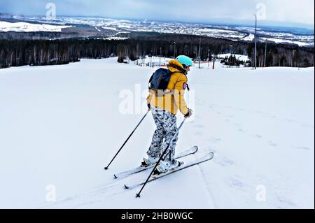 Junge Frau in gelber Jacke und Skihelm Skifahren auf einer Berghang, Wintersport, Alpinski Outdoor-Aktivität, gesunde aktive Lebensweise Stockfoto
