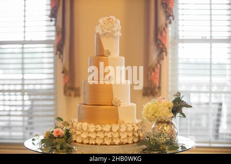 Große fünfstöckige Hochzeitstorte aus Gold und weißem Fondant mit weißem Blumenbelag Stockfoto