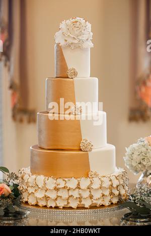 Große fünfstöckige Hochzeitstorte aus Gold und weißem Fondant mit weißem Blumenbelag Stockfoto