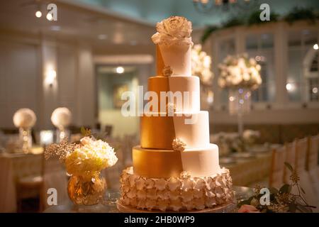 Große fünfstöckige Hochzeitstorte aus Gold und weißem Fondant mit weißem Blumenbelag Stockfoto