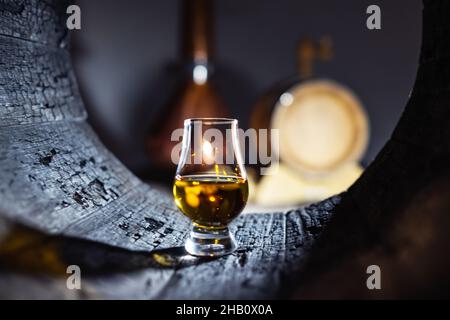 Ein Glas Whiskey im alten Eichenfass. Kupfer-Alambic auf dem Hintergrund. Traditionelles Konzept der Alkoholbrennerei Stockfoto