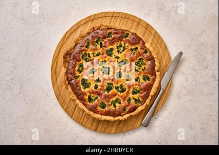 Quiche Pie mit Brokkoli, Thunfisch und Käse auf runder Holzschneidebrett mit Messer. Draufsicht, Kopierbereich Stockfoto