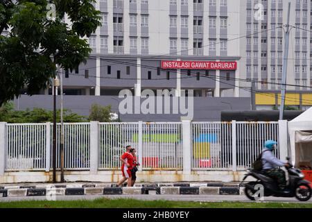 Jakarta, Jakarta. 16th Dez 2021. Maskierte Menschen kommen am 16. Dezember 2021 am Notkrankenhaus Wisma Atlet, einem Krankenhaus für COVID-19-Patienten, in Jakarta, Indonesien vorbei. Indonesien hat seinen ersten Fall von Omicron-Variante in einem Reinigungsdienst in einem Krankenhaus für COVID-19-Patienten in der Hauptstadt Jakarta entdeckt, sagte Gesundheitsminister Budi Gunadi Sadikin am Donnerstag. Quelle: Xu Qin/Xinhua/Alamy Live News Stockfoto