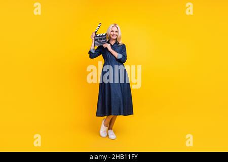 Foto von entzückenden niedlichen pensionierten Frau tragen Jeans Kleidung hält clapperboard isoliert gelbe Farbe Hintergrund Stockfoto