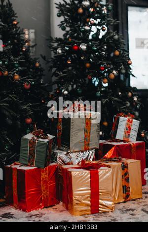 Goldenes, rotes und silbernes Neujahrsgeschenk mit Band unter dem Weihnachtsbaum. Festliches Weihnachtskonzept und Geschenke Stockfoto