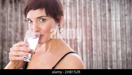 Zusammengesetztes Bild einer kaukasischen Frau, die Wasser aus einem Glas vor einem hölzernen Hintergrund trinkt Stockfoto