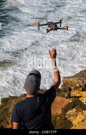 NAZARE, PORTUGAL - 12. Nov 2021: Eine vertikale Aufnahme eines Mannes, der nach einer DJI-Drohne greift, nachdem er sie über die Wellen in Nazare, Portugal, geflogen hat Stockfoto