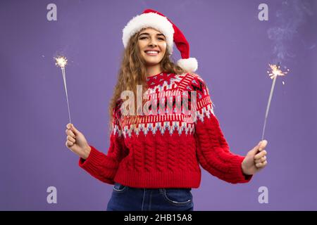 Lächelnd beaty Santa lockige junge Frau hält brennende Wunderkerzen im Studio auf violettem Hintergrund aufgenommen Stockfoto