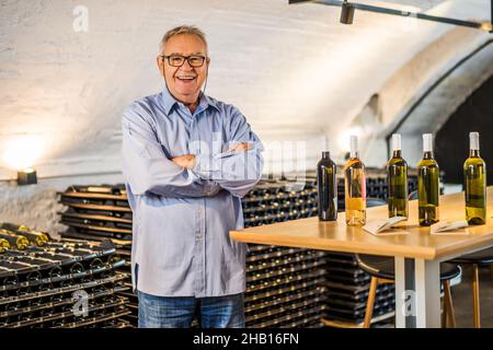 Porträt eines glücklichen älteren Mannes, dem das Weingut gehört. Er steht in seinem Weinkeller. Industrie Weinherstellung Konzept. Stockfoto