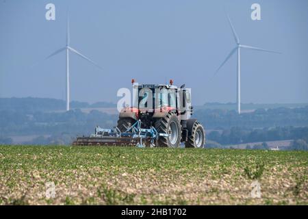 Traktor, der Boden und Windmühlen in der Ferne in Puyrolland (Mittelwestfrankreich) umdreht: Traktor mit Egge auf einem Feld Stockfoto