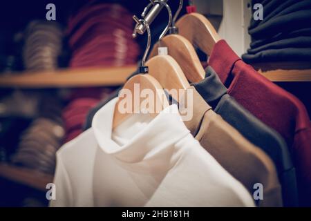 Pullover an Kleiderbügeln. Einkaufen im Geschäft. Kleidung an Kleiderbügeln im Geschäft zum Verkauf. Hintergrund verwischen. Modische Kleidung in einer Boutique. Verschiedene Kleidung auf m Stockfoto