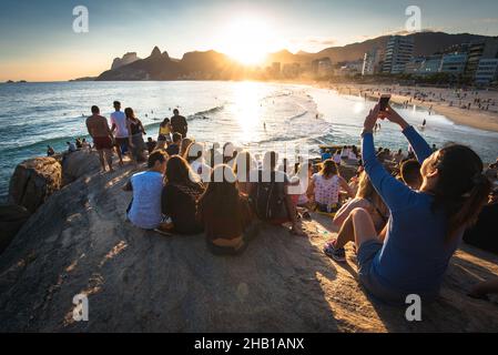 Rio de Janeiro, Brasilien - 18. August 2018: Menschen sitzen überall auf dem Arpoador-Felsen und genießen den wunderschönen Sonnenuntergang. Stockfoto
