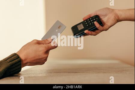 Die Hand einer Frau klopft auf eine Kreditkarte eines kontaktlosen Kartenlesers. Nicht erkennbare weibliche Kundin, die am Checkout-Schalter mit einer Kreditkarte bezahlt. Stockfoto