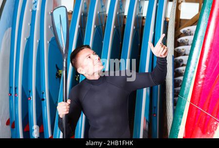 Porträt eines jungen Sportmanns im Neoprenanzug mit Paddel im Surfclub Stockfoto