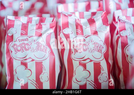 Viele Reihen Popcorn in weißen Papiertüten mit roten vertikalen Streifen und Aufdruck „Fresh Popcorn“ auf den Tüten