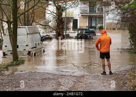 Pamplona, Spanien - 10. Dezember 2021 - Mann schaut auf ein überflutetes Haus und Fahrzeuge. Stockfoto