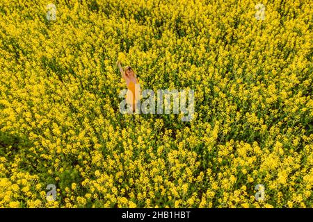 Frau in gelbem Kleid auf blühendem Rapsfeld. Leuchtend gelbe Blumen und glückliche Frau Stockfoto