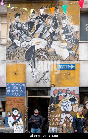 2. November 2021, Orgosolo, Nuoro, Italien: Im Dorf Orgosolo auf Sardinien stehen Menschen vor einer Wand mit Wandmalereien.das Dorf Orgosolo auf Sardinien hat eine lange Tradition der politischen Straßenkunst, die an den Wänden des Dorfes sichtbar ist. Seit einigen Jahren verbinden sich die linksextremen Fresken und die Hommage an die Kämpfe des Volkes mit Gemälden zum Thema Migranten und das Coronavirus. (Bild: © Laurent Coust/SOPA Images via ZUMA Press Wire) Stockfoto