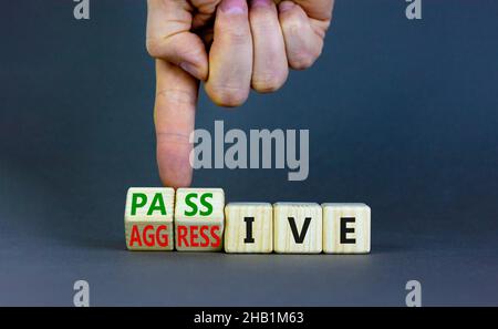 Passives oder aggressives Symbol. Geschäftsmann dreht Holzwürfel und ändert das Wort passiv in aggressiv. Schöner grauer Hintergrund, Kopierbereich. Bus Stockfoto