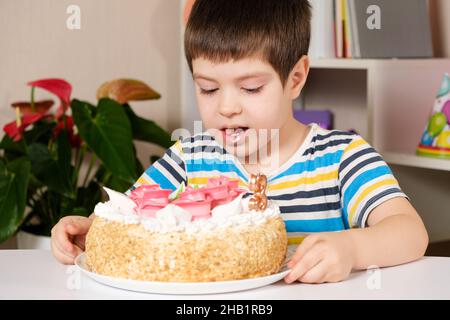 Vorschulkind isst Geburtstagskuchen, leckt und macht einen Wunsch. Stockfoto