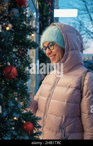 Hübsche Frau in der Nähe beleuchteten Neujahr dekoriert Fenster. Weihnachtsferien oder Shopping auf Neujahr oder Weihnachten Konzept Stockfoto