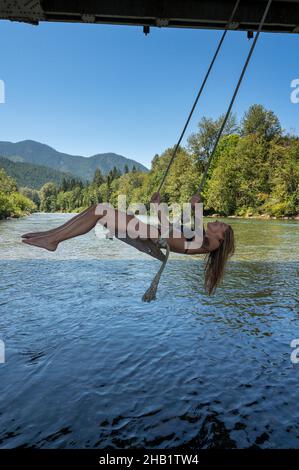 Setzen Sie die Frau im Bikini auf eine Schaukel über einen Fluss in den Bergen Stockfoto