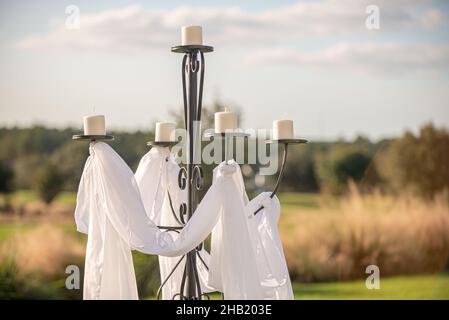 Großer schwarzer Kerzenhalter mit fünf Zapfen, in Weiß mit weißem Kerzendekor bei der Hochzeitszeremonie im Freien drapiert Stockfoto