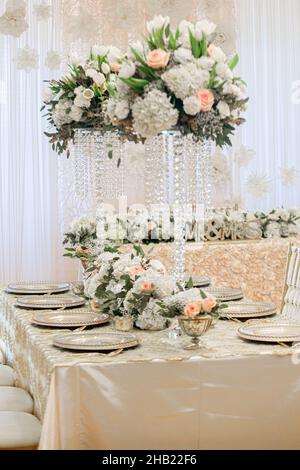 Wunderschöne Tischlandschaft gefüllt mit goldenen Ladegeräten, Blumen und Kristallvasen bei der Hochzeitsfeier Stockfoto