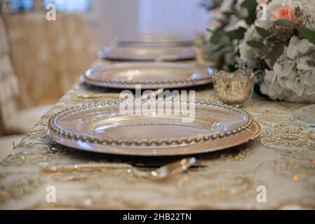 Wunderschöne Tischlanscape Reihen sich auf goldene Ladeteller und Blumen auf goldenen Paisley-Tischlappen beim Hochzeitsempfang Stockfoto