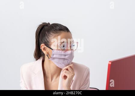 Salisbury, Wiltshire, Großbritannien. 2021. Attraktive Frau trägt rosa Gesichtsmask und mit einem Computer und Tastatur. Stockfoto