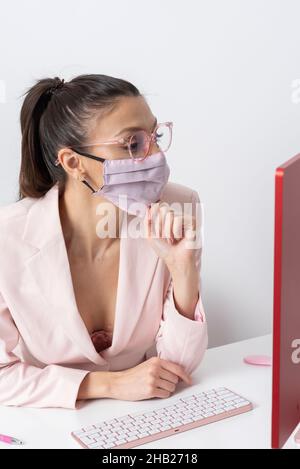 Salisbury, Wiltshire, Großbritannien. 2021. Attraktive Frau trägt rosa Gesichtsmask und mit einem Computer und Tastatur. Stockfoto