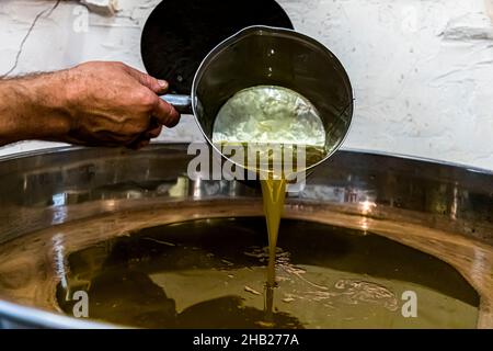 Pressemeister Fabrice Godet gießt frisch geschäumtes, goldgelbes Olivenöl durch ein Metallsiebe in einen großen Edelstahlbehälter im Olivenölmuseum Moulin de Saint-Cassien in Draguignan, Département Var, Frankreich; nach dem Pressen steht die Wasser-Öl-Mischung etwa eine Stunde unbedeckt, bevor er das oben schwimmende Öl abschöpft – das schwerere Fruchtwasser sinkt auf den Boden. Stockfoto
