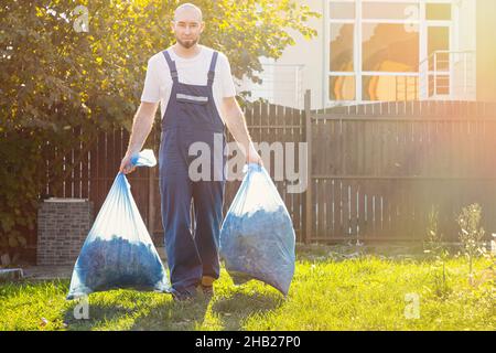 Der Gärtner lächelt und entfernt die Beutel mit Kompost. Leicht. Blaue Uniform. Stockfoto