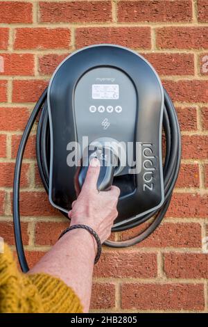 Frau, die ein Ladegerät für Elektroautos von Zappi verwendet, das an der Außenwand einer privaten Garage befestigt ist. Stockfoto