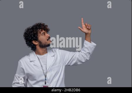 Fokussierter männlicher Arzt mit einem angehobenen Zeigefinger, der nach oben starrt Stockfoto